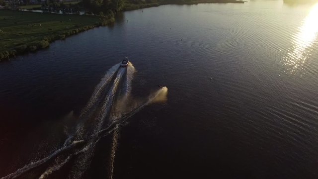 Beautiful drone view of a monoskier slalomming behind a waterski boat during the sunrise on a lake in Holland