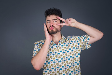 Leisure lifestyle people person celebrate flirt coquettish concept. Handsome pretty cheerful blond man making v-sign near eyes wearing casual clothes standing against gray wall.