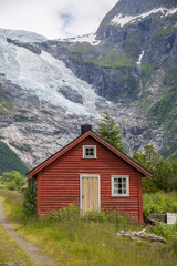 Fototapeta na wymiar Abandoned village with different colored wooden houses in an idyllic location, between mountains, glacier in the background, abundant green vegetation on a summer day in Norway