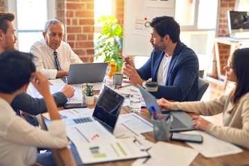 Group of business workers working together. Sitting on desk using laptop and talking at the office