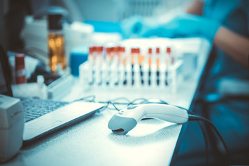 Bar codes scanner, blood sample tubes and laptop with lab technician hands on background....