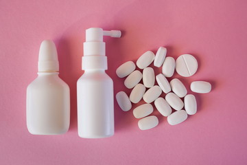 White oval tablets and spray bottles on a pink background. Cold treatment concept