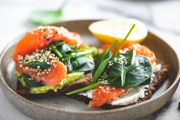 Rye bread toast with avocado, salmon, cream cheese, spinach leaf and hemp seeds on plate. Healthy food. Appetizer, breakfast or snack