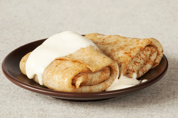 Tasty stuffed pancakes with sour cream on a plate close-up.