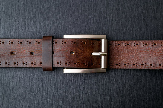 Brown genuine leather belt with classic metal buckle on a black background. Men's stylish leather accessories. Low key image.