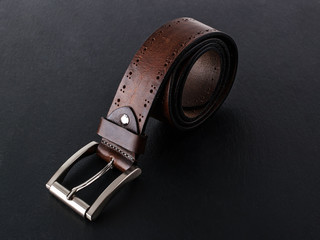 Brown belt made of genuine leather with classic metal buckle on a black surface. Men's stylish...