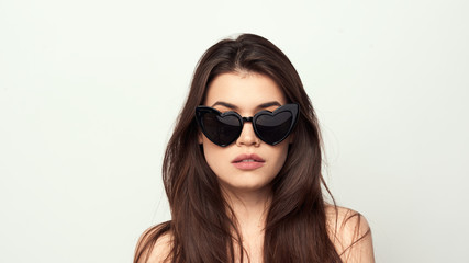 beautiful young girl with brown hair in fashionable glasses posing on a white background with bare shoulders, empty space for text