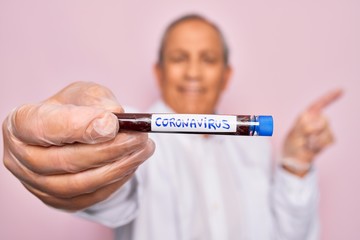 Senior handsome hoary man holding coronavirus tube test over isolated pink background very happy pointing with hand and finger to the side