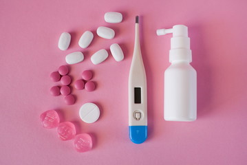 The concept of treatment and protection of the disease, colds and coronavirus. Antibiotic and spray for the throat and thermometer on a pink background.