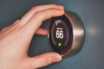 Hand operating smart thermostat to save money