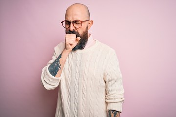 Handsome bald man with beard and tattoo wearing glasses and sweater over pink background feeling unwell and coughing as symptom for cold or bronchitis. Health care concept.