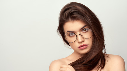beautiful young girl with brown hair in fashionable glasses posing on a white background with bare shoulders, empty space for text