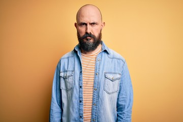 Handsome bald man with beard wearing casual denim jacket and striped t-shirt skeptic and nervous, frowning upset because of problem. Negative person.