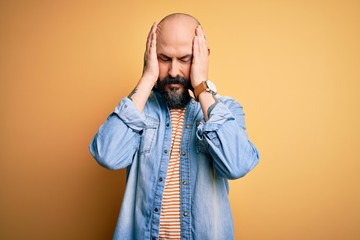 Handsome bald man with beard wearing casual denim jacket and striped t-shirt suffering from headache desperate and stressed because pain and migraine. Hands on head.