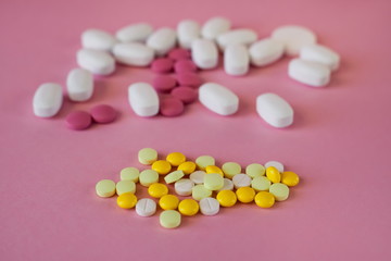 Assorted pharmaceutical medicine pills. Multi-colored pills of different shapes on a light pink background, foreground of white and yellow pills, selective focus.