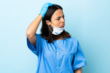 Surgeon woman over isolated blue background having doubts while scratching head