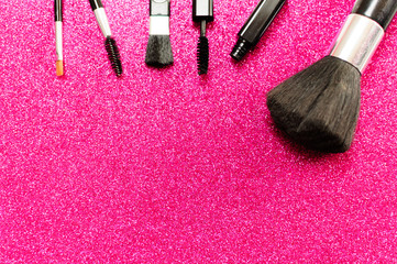 Makeup brush and decorative cosmetics on a pink background.