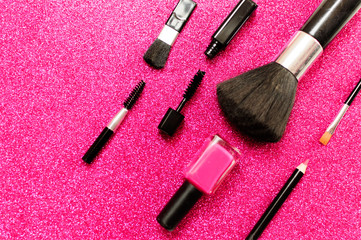 Makeup brush and decorative cosmetics on a pink background.