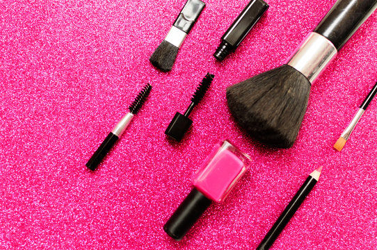 Makeup brush and decorative cosmetics on a pink background.