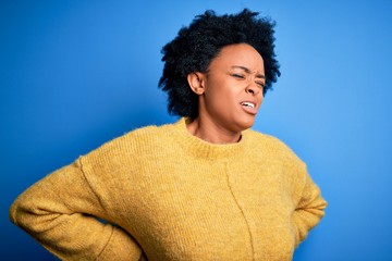 Young beautiful African American afro woman with curly hair wearing yellow casual sweater Suffering of backache, touching back with hand, muscular pain