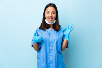 Surgeon woman over isolated blue background showing ok sign and thumb up gesture