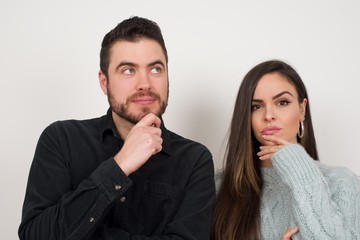 Shot of contemplative thoughtful Young woman keeps hand under chin, looks thoughtfully upwards, dressed in casual clothes, poses over white background with free space for your text