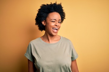 Young beautiful African American afro woman with curly hair wearing casual t-shirt winking looking...
