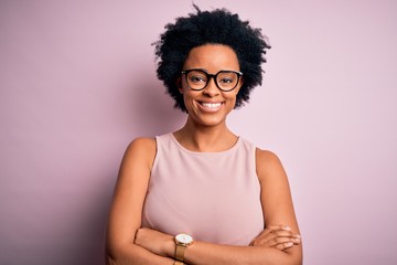 Young beautiful African American afro woman with curly hair wearing t-shirt and glasses happy face smiling with crossed arms looking at the camera. Positive person. - obrazy, fototapety, plakaty
