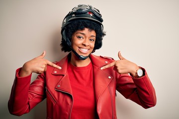 Young African American afro motorcyclist woman with curly hair wearing motorcycle helmet looking confident with smile on face, pointing oneself with fingers proud and happy.