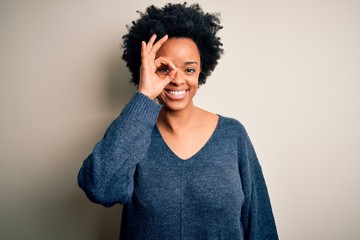 Fototapeta na wymiar Young beautiful African American afro woman with curly hair wearing casual sweater doing ok gesture with hand smiling, eye looking through fingers with happy face.