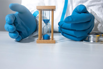 A doctor in a protective suit held a fragile hourglass together with two blue gloved hands