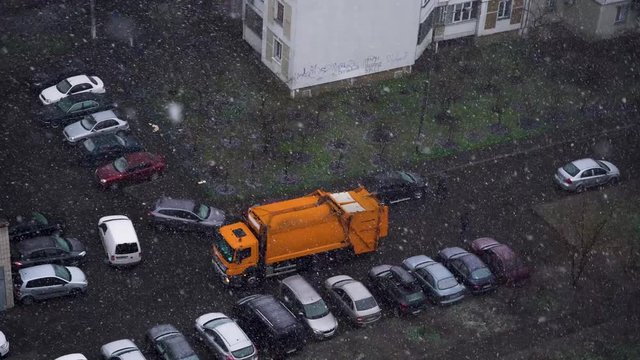 A garbage truck drives into the yard to pick up the garbage bins. Snowstorm in the city in spring