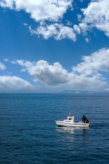 small lonely boat sailing the blue sea, mountains in the background and wonderful clouds