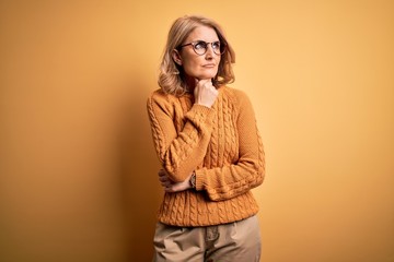 Middle age beautiful blonde woman wearing casual sweater and glasses over yellow background Touching painful neck, sore throat for flu, clod and infection