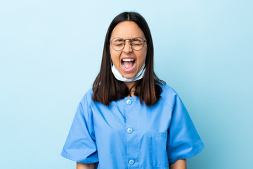 Surgeon woman over isolated blue background shouting to the front with mouth wide open