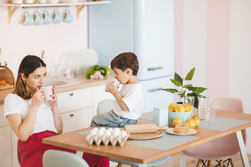 Young mother having breakfast in kitchen with her little son.