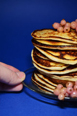 stack of pancakes on a blue background with berries and a hand