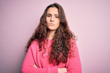 Young beautiful woman with curly hair wearing casual sweater over isolated pink background skeptic...