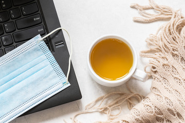 Distance work and education concept. Cup of herbal tea, cozy blanket, lap top and surgical mask top view. Quarantine and epidemic prevention concept.