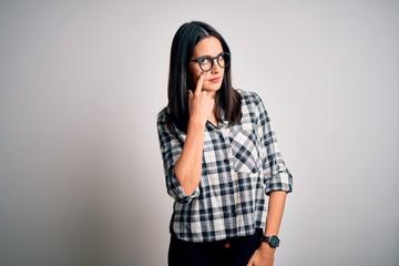 Young brunette woman with blue eyes wearing casual shirt and glasses over white background Pointing to the eye watching you gesture, suspicious expression