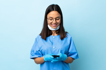 Surgeon woman over isolated blue background sending a message with the mobile
