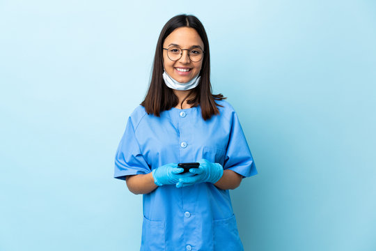 Surgeon woman over isolated blue background sending a message with the mobile