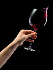 Woman hand holding red wine glass with splashes isolated on black.