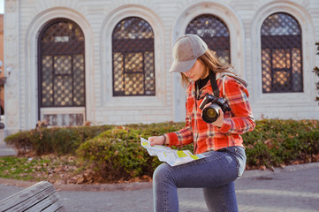 Obraz premium Girl with a map and a camera. Woman traveling and taking pictures outdoors. Photographer Traveling Attractions Walk Hobby Vacation Concept. Nice day in Europe.