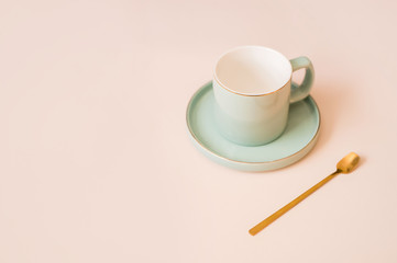 A beautiful coffee cup with a saucer and a golden spoon on a light background.