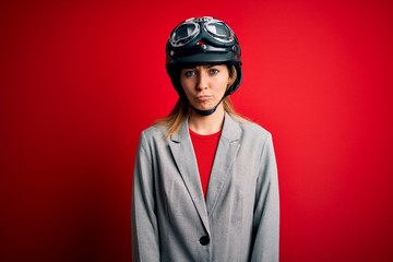 Young beautiful blonde motorcyclist woman wearing motorcycle helmet over red background depressed and worry for distress, crying angry and afraid. Sad expression.