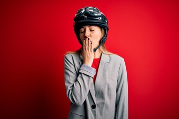 Young beautiful blonde motorcyclist woman wearing motorcycle helmet over red background bored yawning tired covering mouth with hand. Restless and sleepiness.