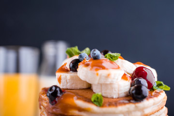 Delicious pancakes with banana, berries, mint and salted caramel in a plate.