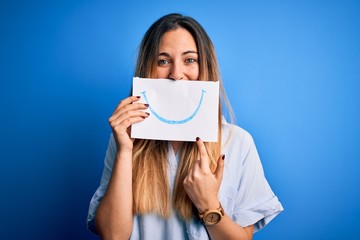 Fototapeta premium Young beautiful brunette woman holding card with smile illustration on mouth very happy pointing with hand and finger