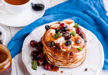 Delicious pancakes with banana, berries, mint and salted caramel in a plate.
